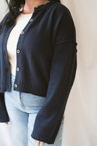 Model wearing the navy full button raw edge cardigan. Styled fully unbuttoned over a cream tank and paired with basic denim jeans. 