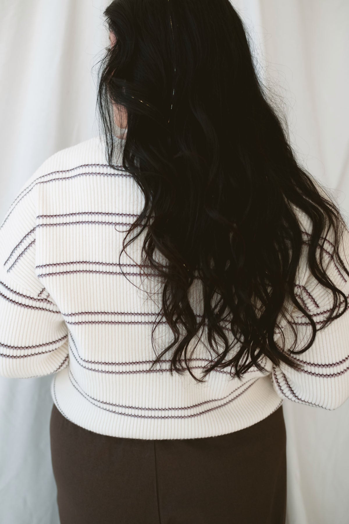 Model wearing a knit striped sweater in cream with burgundy. 