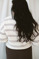 Model wearing a knit striped sweater in cream with burgundy. 