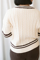 Charlotte cream cable knit V-neck varsity sweater with chocolate brown accents and classic collegiate-inspired details.