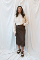 Model wearing a round neck solid sweater in light taupe. Styled with a brown satin skirt with lace trim.