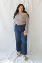 Model wearing the asymmetrical off the shoulder striped top with a pair of basic dark denim and a pop of color in the necklace. Top has lettuce hem detail on the sleeves and a fitted look. 