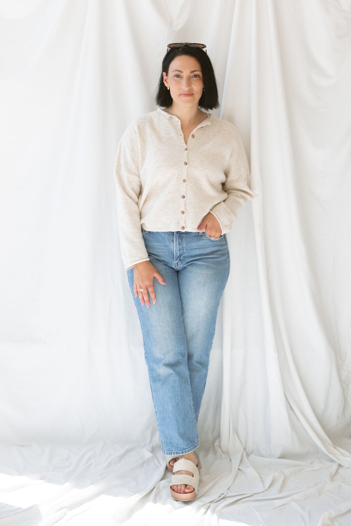 Model wearing button up cardigan in color oat. This cardigan is easy to wear open and layered over a variety of tanks and shirts or you can wear it buttoned up as a top. Model has cardigan fully buttoned and paired with jeans and oat colored sandals. 