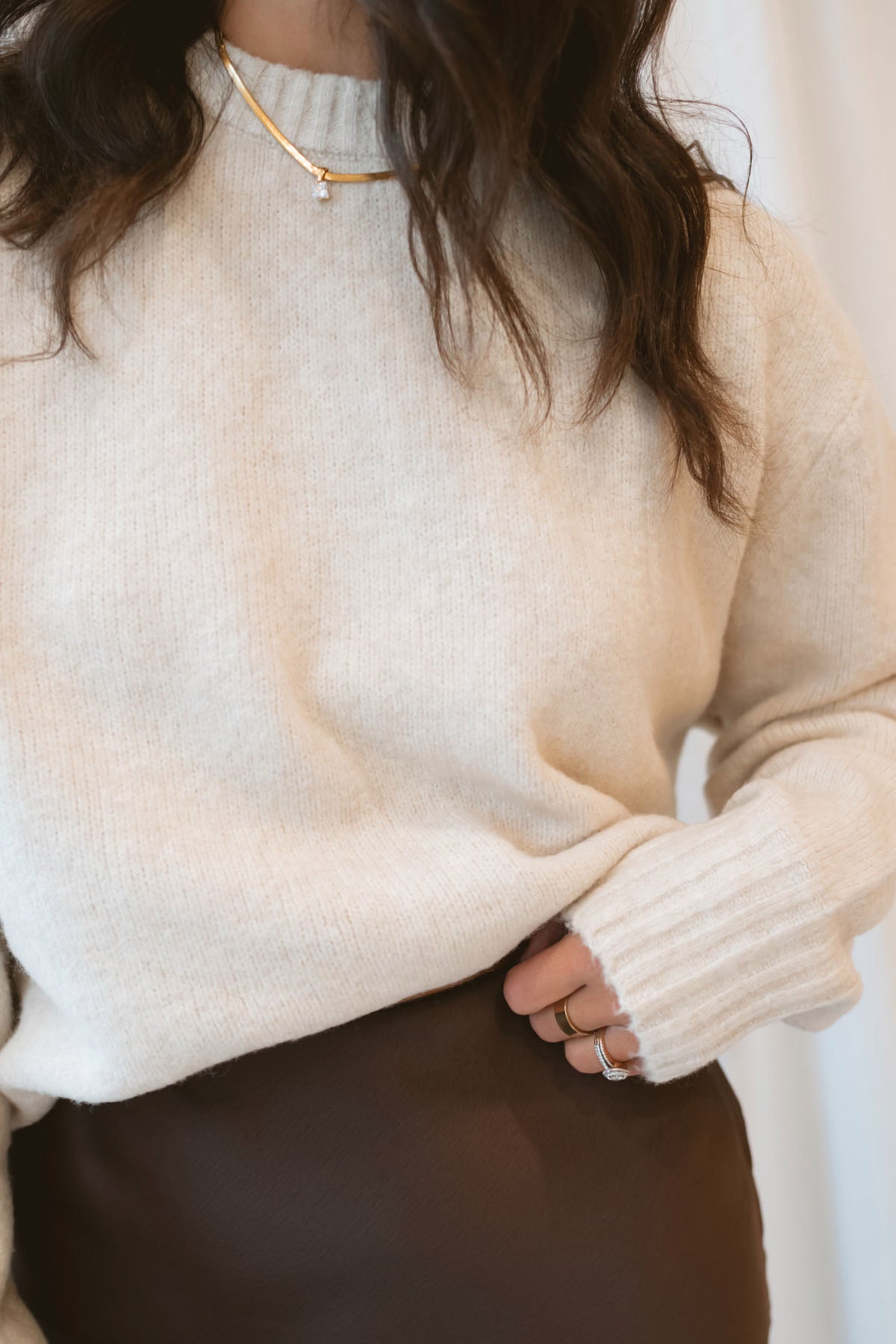 Model wearing a round neck solid sweater in light taupe. Styled with a brown satin skirt with lace trim.