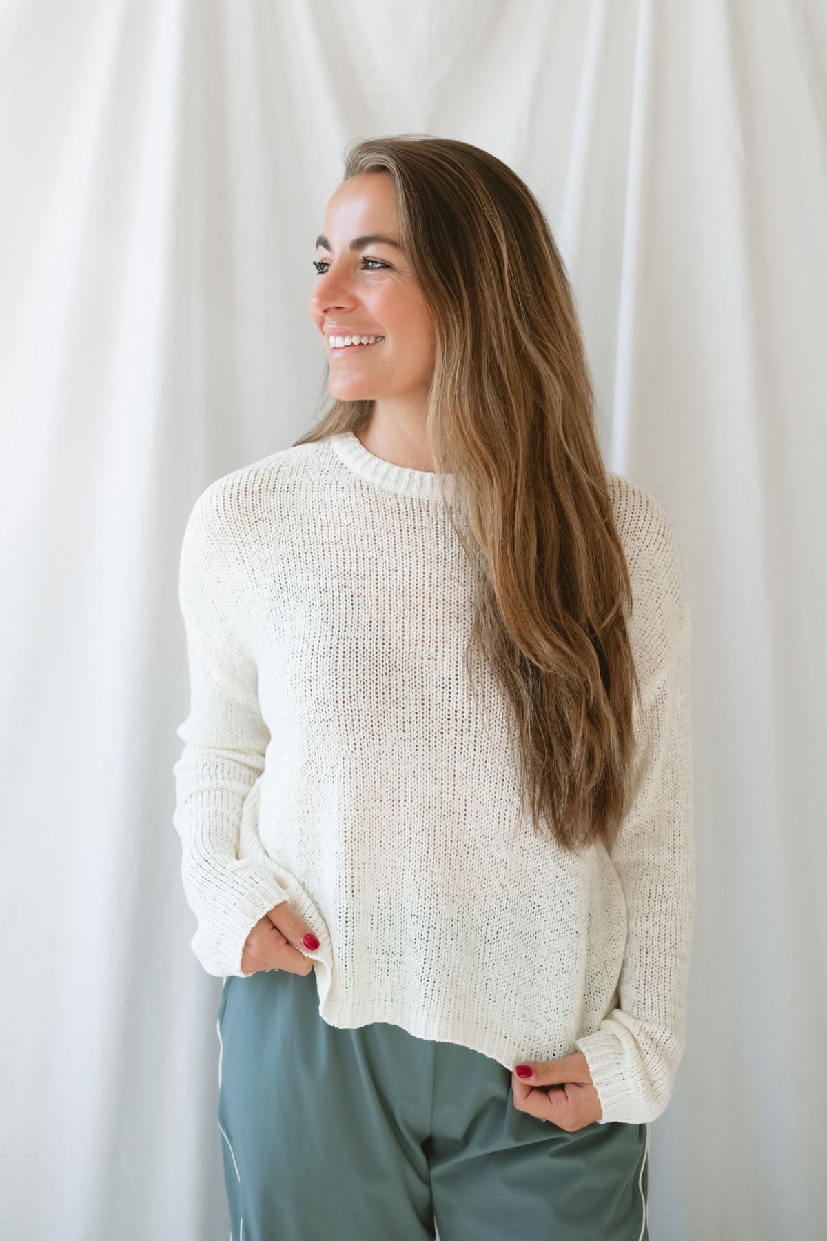Model is wearing a lightweight round neck sweater in an ivory color. 