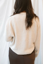 Model wearing a round neck solid sweater in light taupe. Styled with a brown satin skirt with lace trim.