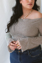 Model wearing the asymmetrical off the shoulder striped top with a pair of basic dark denim and a pop of color in the necklace. Top has lettuce hem detail on the sleeves and a fitted look. 