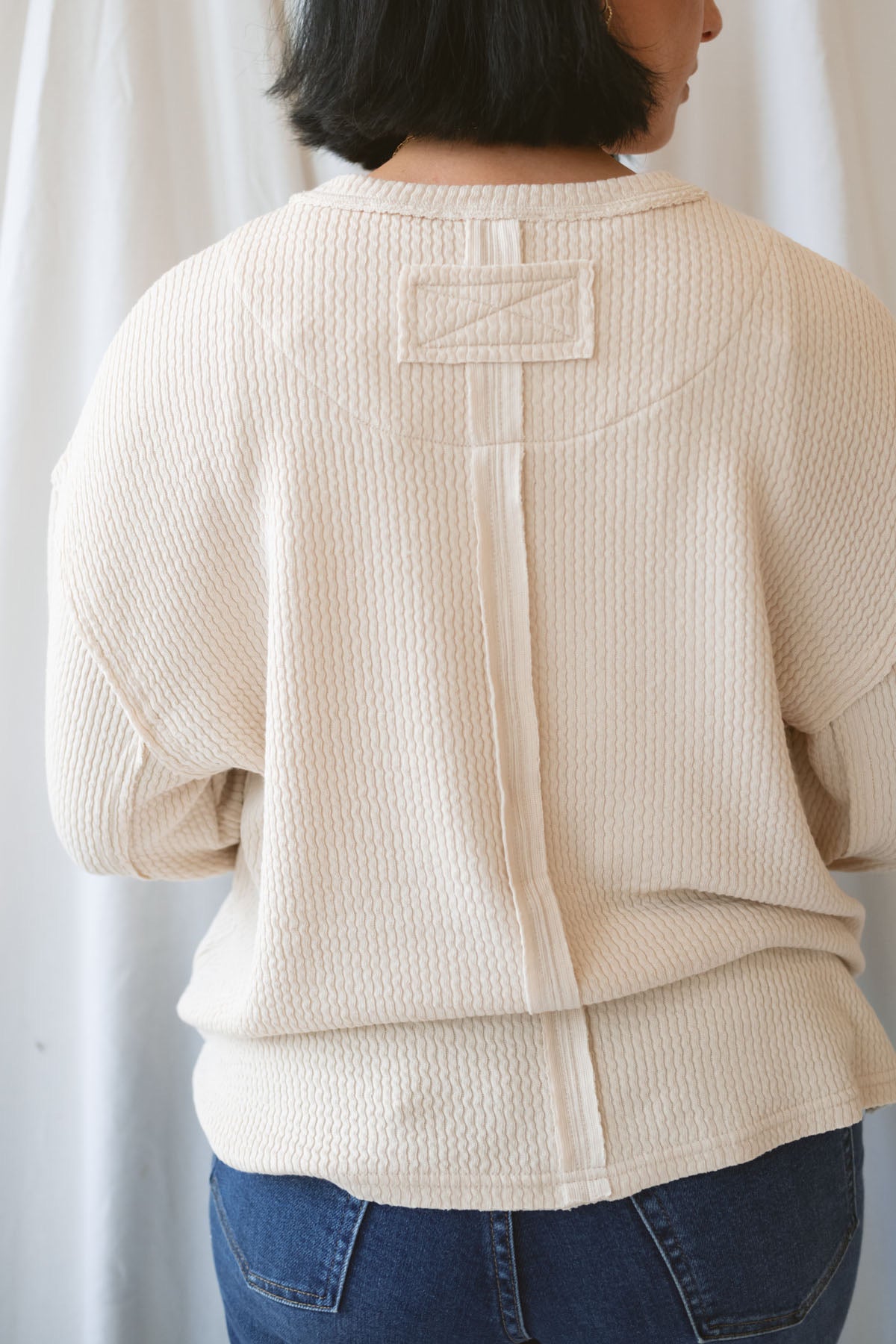 Model wearing a textured exposed seam long sleeve top in a natural color.