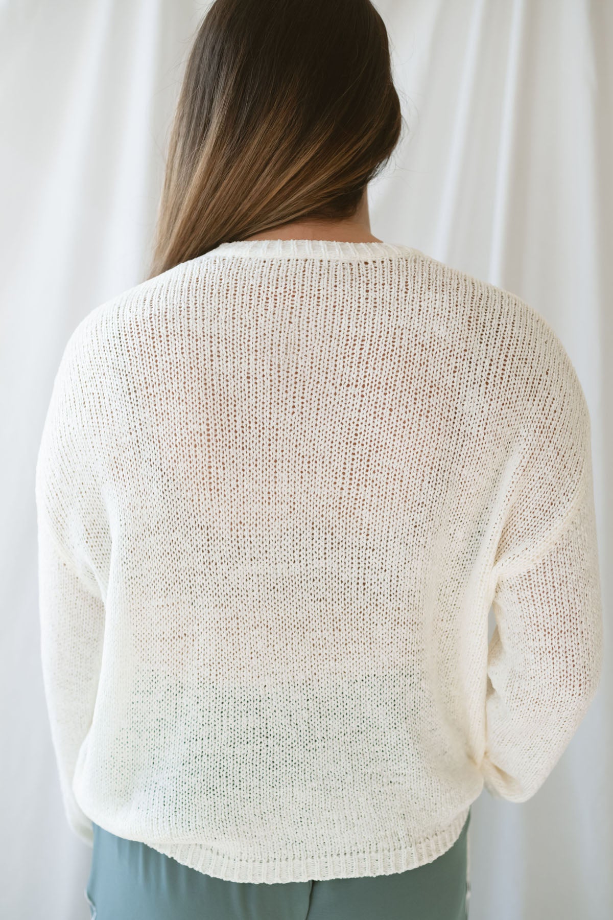 Model is wearing a lightweight round neck sweater in an ivory color. 