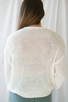 Model is wearing a lightweight round neck sweater in an ivory color. 