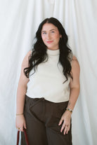 Model wearing sleeveless beige turtleneck. 