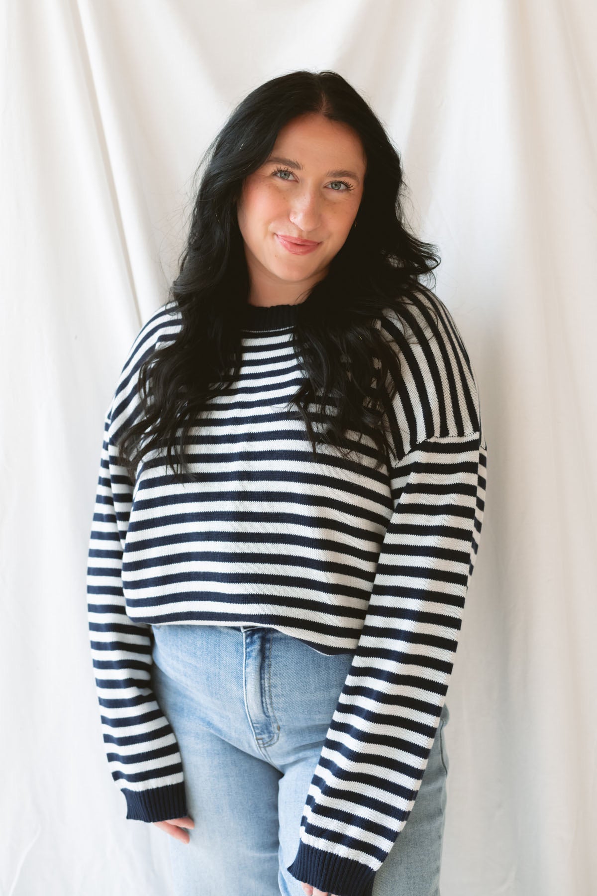 Model wearing striped lightweight sweater with back button detail. Hem stands out with a thicker band of the deep navy, contrasting the white beautifully. Model has sweater pairs with a classic pair of jeans. 