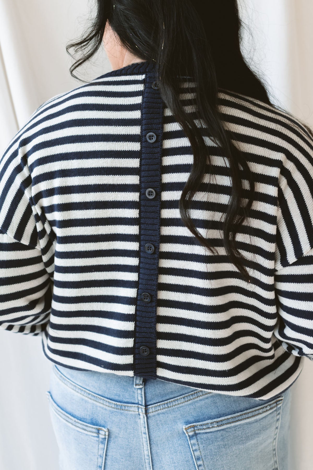 Back view of model wearing the striped lightweight sweater. Highlighting the back button detail of the sweater.