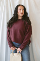 Model is wearing raw edge extended shoulder sweater in the deep maroon color. 