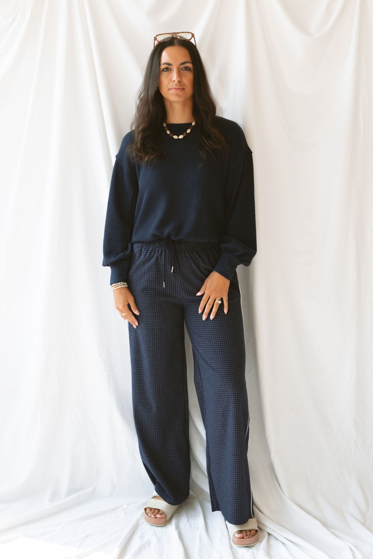 Model wearing textured exposed seam long sleeve top in color Navy. A great basic to dress up or down with a variety of pant styles. Model styled with our checkered drawstring waist pants in navy for a beautiful Monochromatic color combination and comfortable feel.