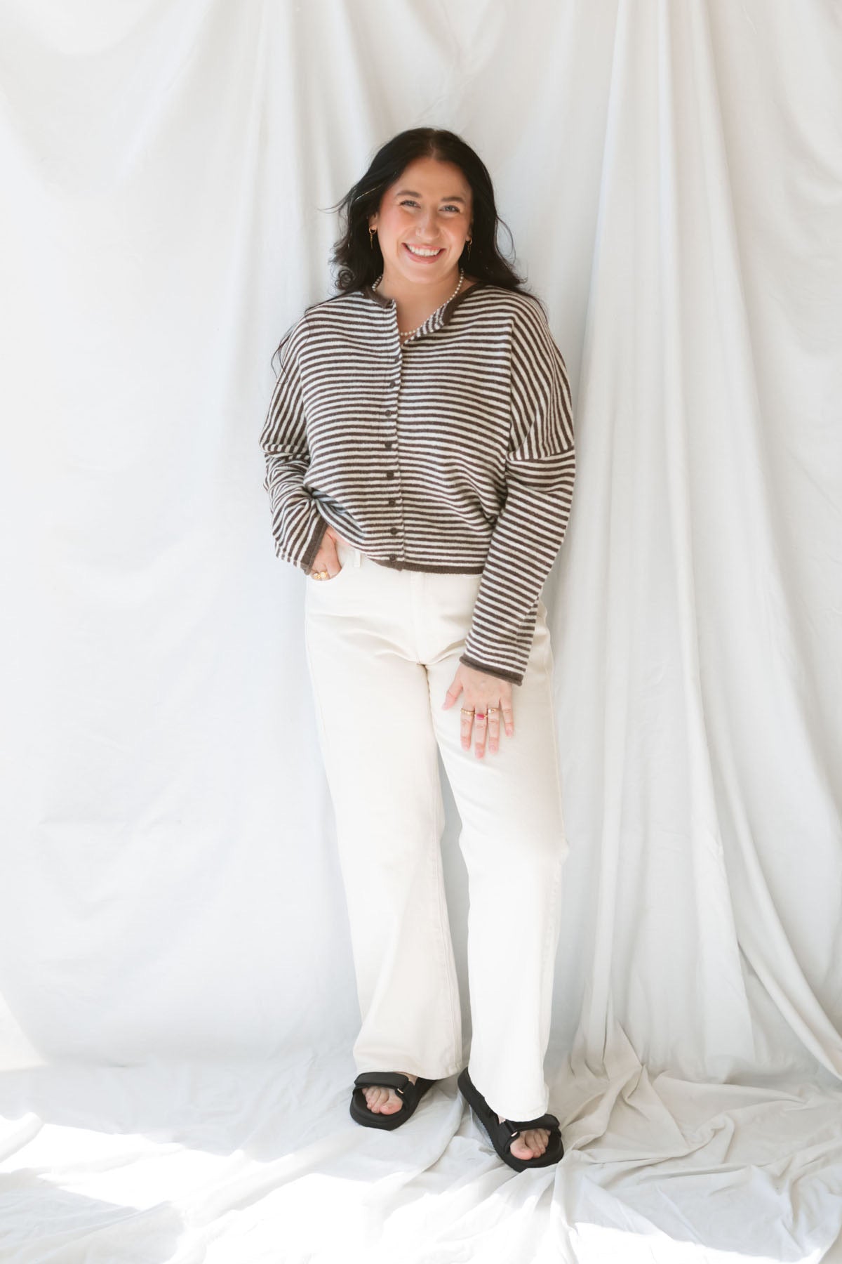 Close up view of model wearing the stripe drop shoulder long sleeve cardigan. This cardigan layers well over many tanks and shirts or you can wear it fully buttoned up as a top. Easy to transition form season to season. Model has cardigan styled as a shirt and paired with a pair of cream denim pants. 