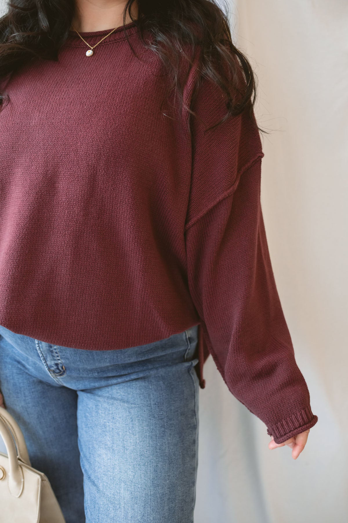Model is wearing raw edge extended shoulder sweater in the deep maroon color. 