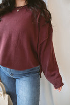 Model is wearing raw edge extended shoulder sweater in the deep maroon color. 