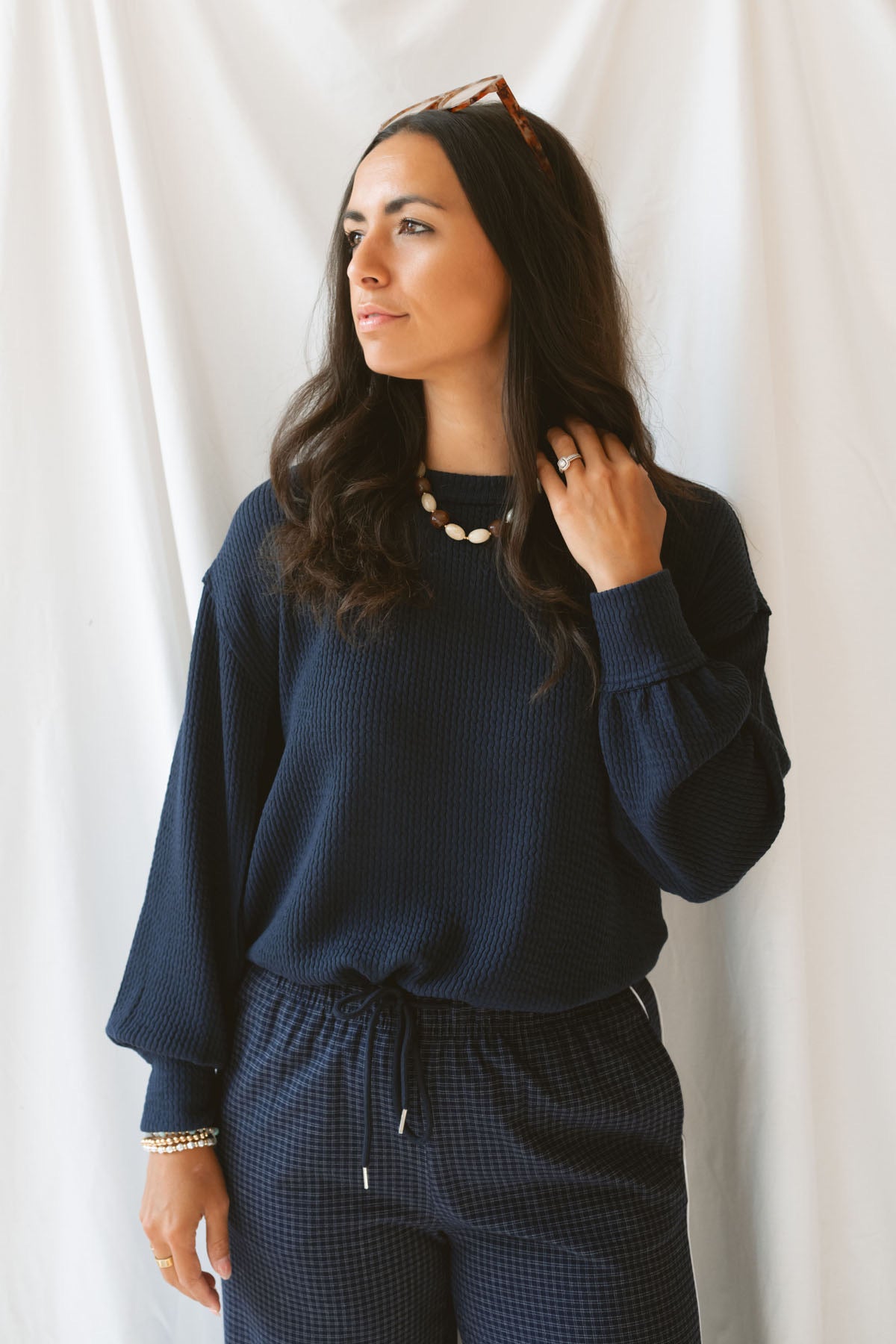 Model wearing textured exposed seam long sleeve top in color Navy. A great basic to dress up or down with a variety of pant styles. Model styled with our checkered drawstring waist pants in navy for a beautiful Monochromatic color combination and comfortable feel.