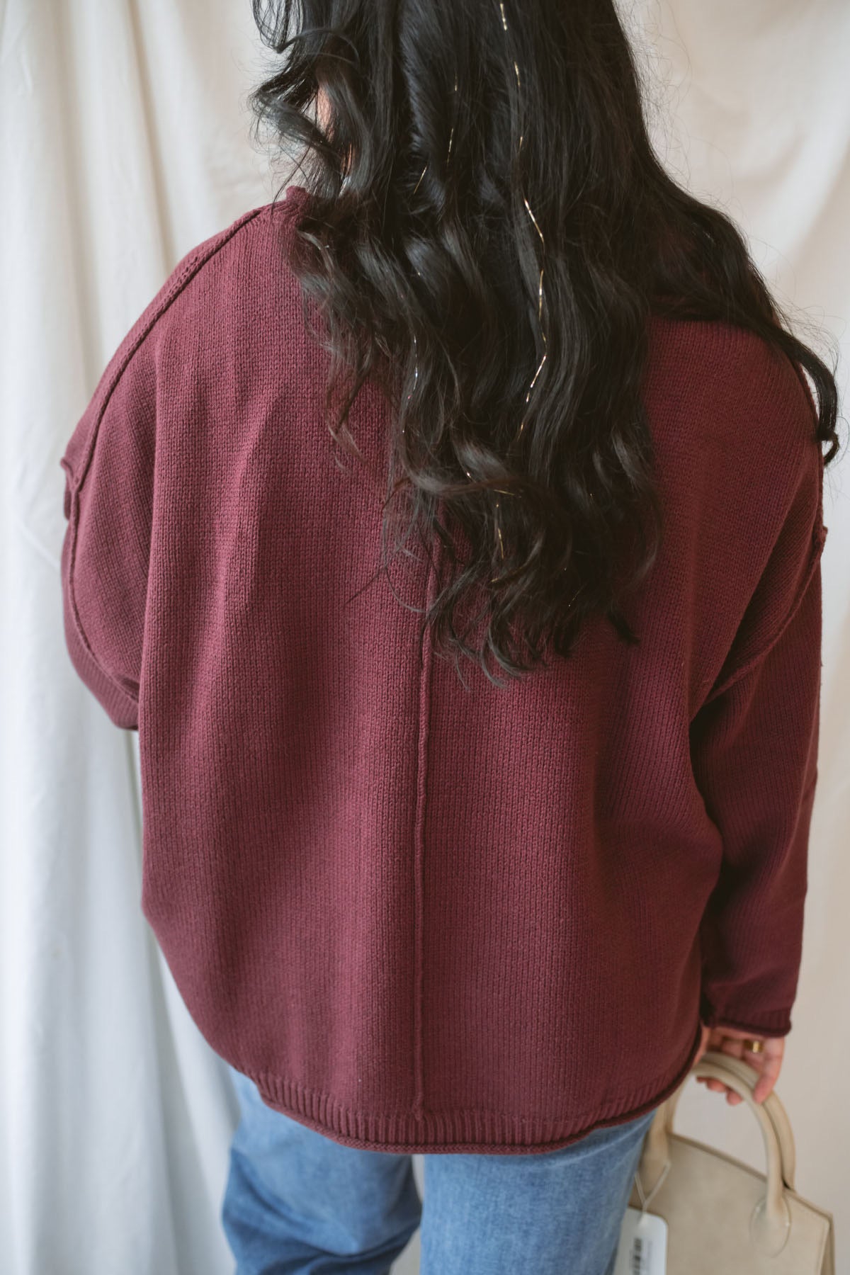 Model is wearing raw edge extended shoulder sweater in the deep maroon color. 