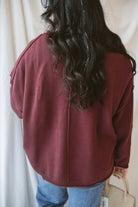 Model is wearing raw edge extended shoulder sweater in the deep maroon color. 