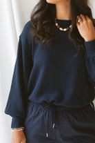 Model wearing textured exposed seam long sleeve top in color Navy. A great basic to dress up or down with a variety of pant styles. Model styled with our checkered drawstring waist pants in navy for a beautiful Monochromatic color combination and comfortable feel.