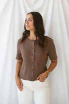 Model is wearing the ribbed short sleeve cardigan in brown. Model has it paired with an off white denim pant for a cassic and timeless look.