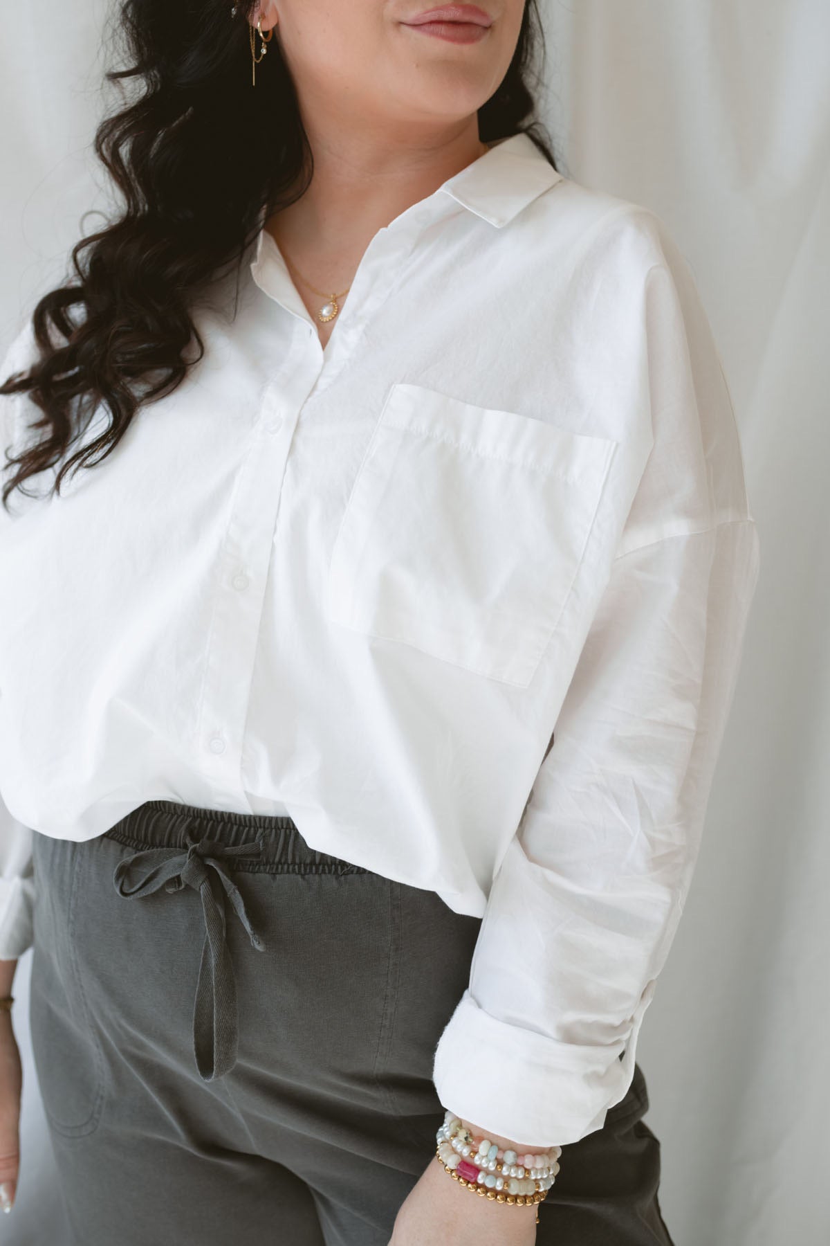 Close up of model wearing the long sleeve white button up top. Model has shirt styled fully buttoned and tucked into the Mila wide leg pants. This outfit is easy and casual but still feels put together. 