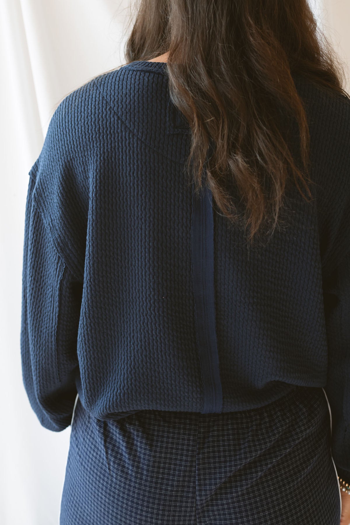 Back view of model wearing textured long sleeve top in color Navy. Back side featured exposed seam detail