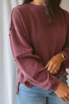 Model wearing exposed seam detail long sleeve top in a light maroon color.