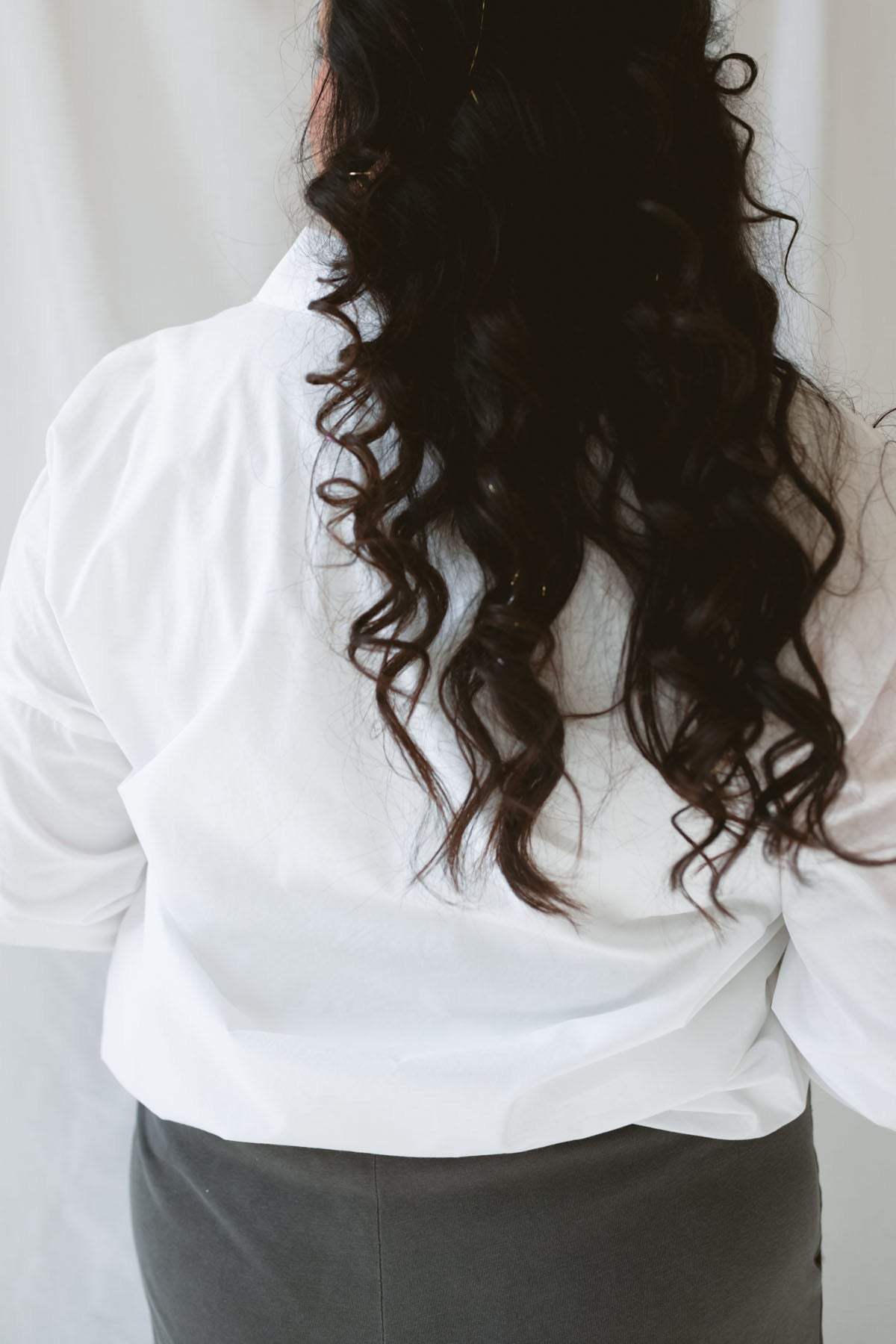 Back view of model wearing the long sleeve white button up top. Model has shirt styled fully buttoned and tucked into the Mila wide leg pants. This outfit is easy and casual but still feels put together. 