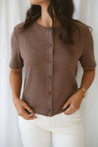 Model is wearing the ribbed short sleeve cardigan in brown. Model has it paired with an off white denim pant for a cassic and timeless look.
