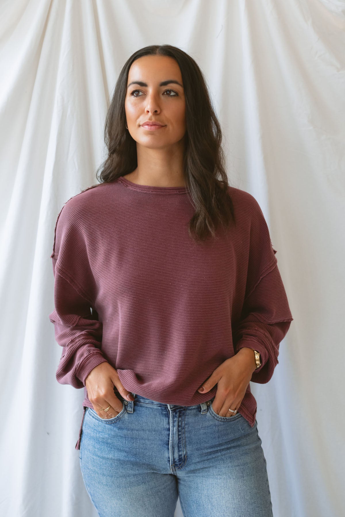 Model wearing exposed seam detail long sleeve top in a light maroon color.