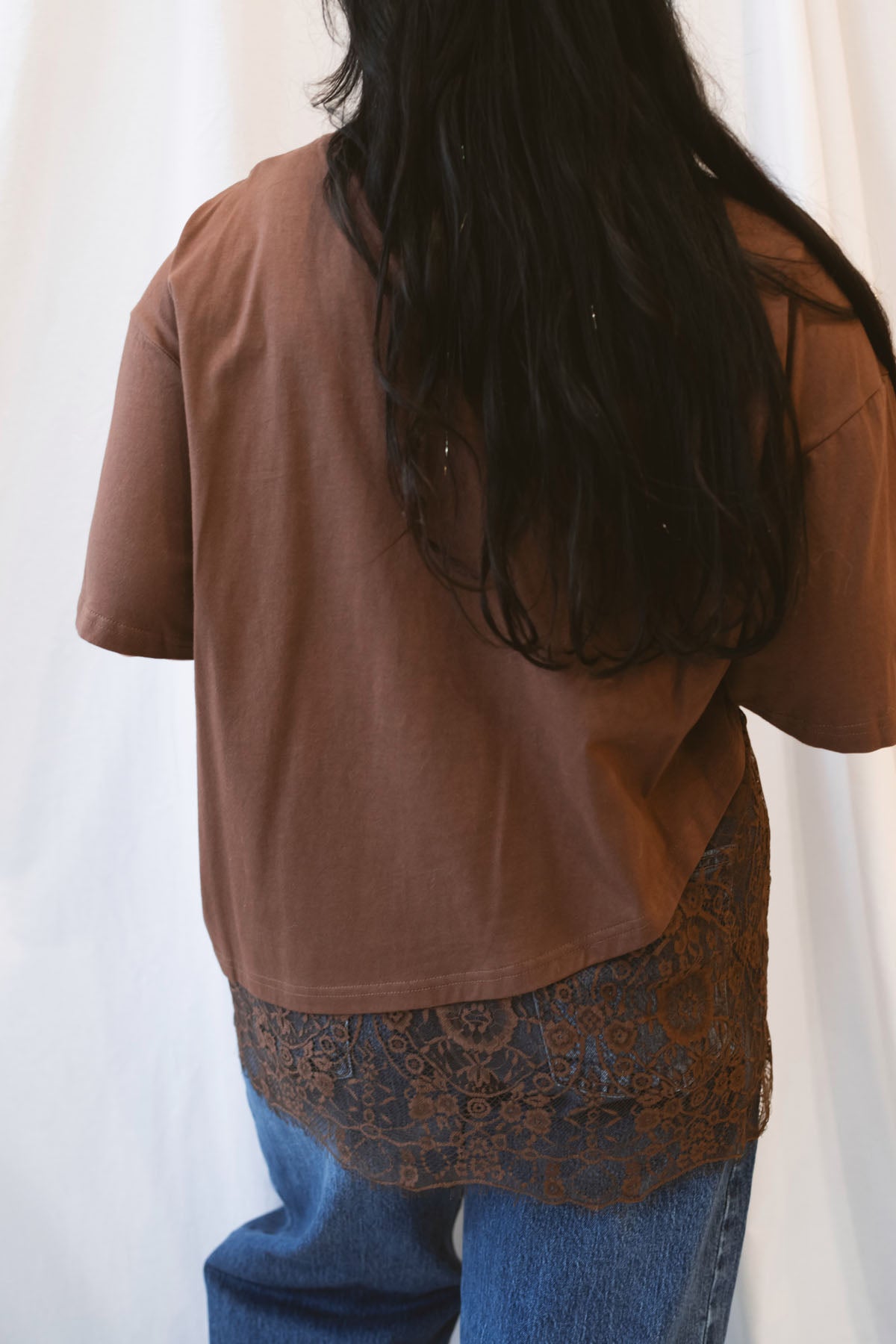 Chocolate brown women's t-shirt featuring delicate floral lace trim and an asymmetrical silhouette for a feminine, elevated everyday look.
