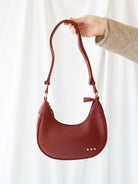 Model holding crescent shaped bag, so you can see strap and front view of bag. 