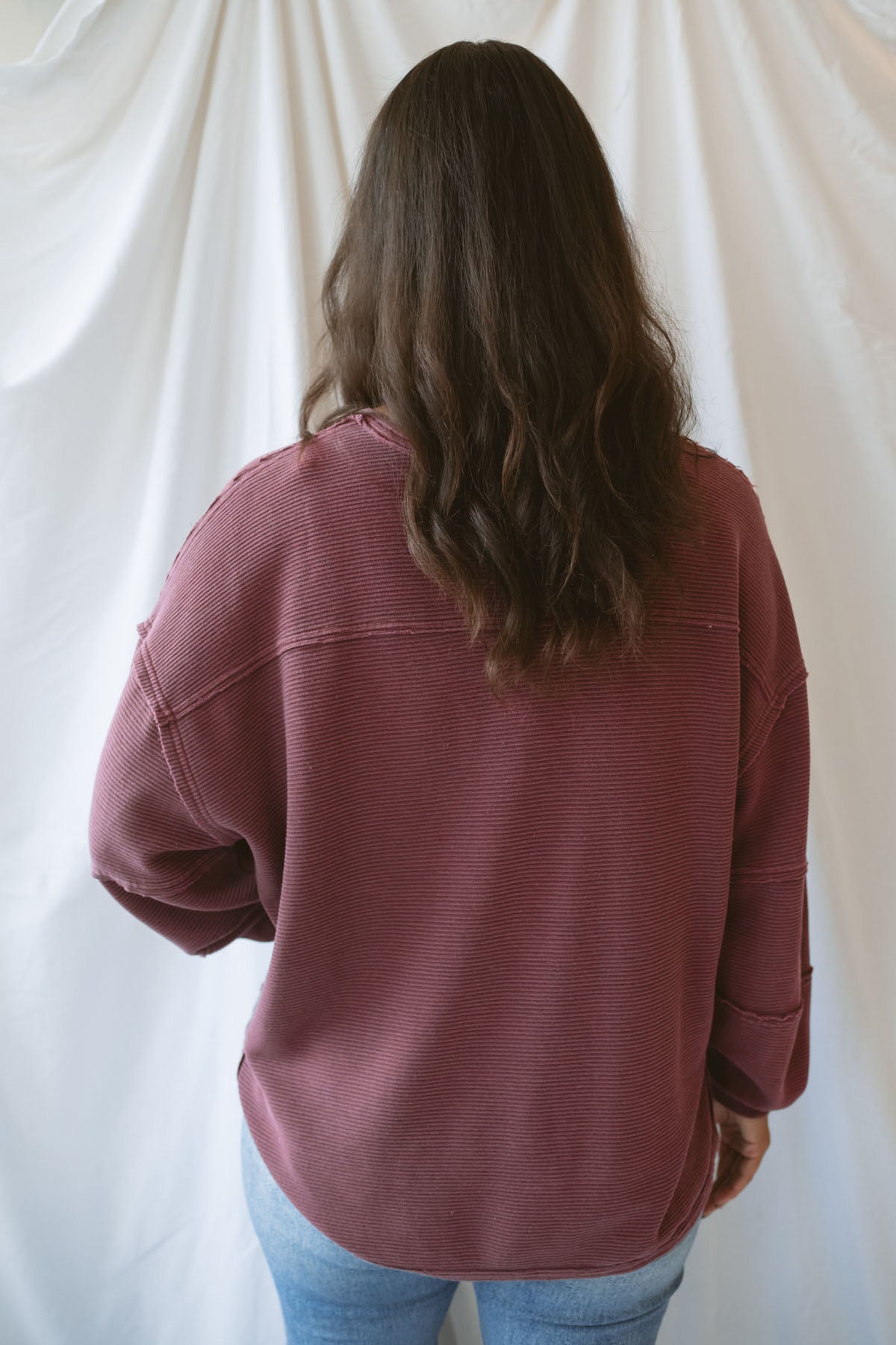 Model wearing exposed seam detail long sleeve top in a light maroon color.
