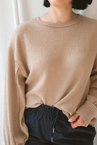 Close up of model wearing textured exposed seam long sleeve top in color khaki. A great basic to dress up or down with a variety of pant styles. Model styled with our checkered drawstring waist pants in navy for a beautiful color combination and comfortable feel.