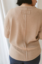 Back view of model wearing textured long sleeve top in color khaki. Details on back include exposed seam.