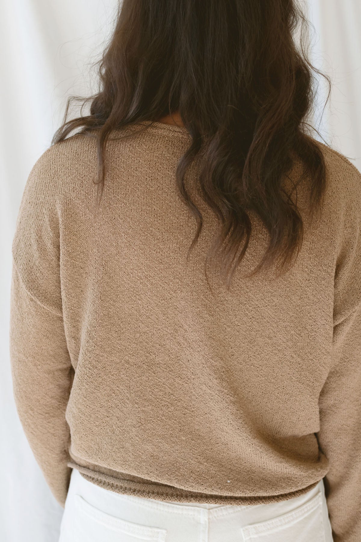 Back view of model wearing long sleeve raw edge knit sweater. Paired with shorts during the summer or pants heading into the cooler seasons makes this a great staple season after season. 