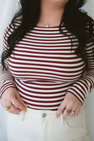 Model wearing long sleeve boat neck style striped top. 