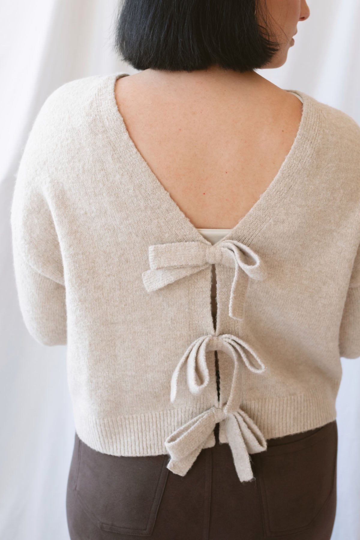 Kayla light taupe knit sweater with a reversible ribbon bow detail, styled with the bow in front.