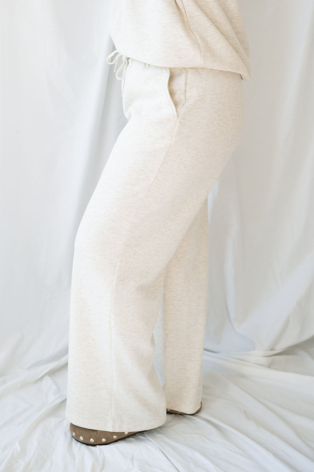 Woman wearing a light beige lounge set with crew neck sweatshirt and drawstring pants on a white background 