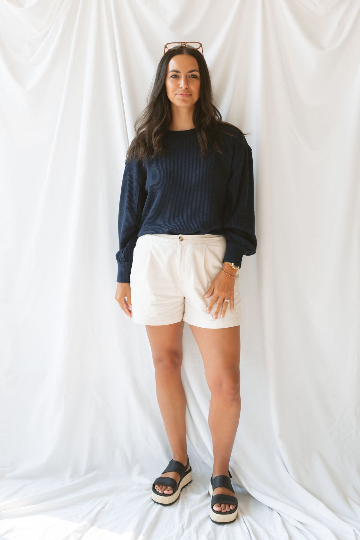Model wearing textured exposed seam long sleeve top in color Navy. A great basic to dress up or down with a variety of pant styles. Model styled with a pair of cream shorts for a more summery look.
