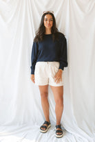 Model wearing textured exposed seam long sleeve top in color Navy. A great basic to dress up or down with a variety of pant styles. Model styled with a pair of cream shorts for a more summery look.