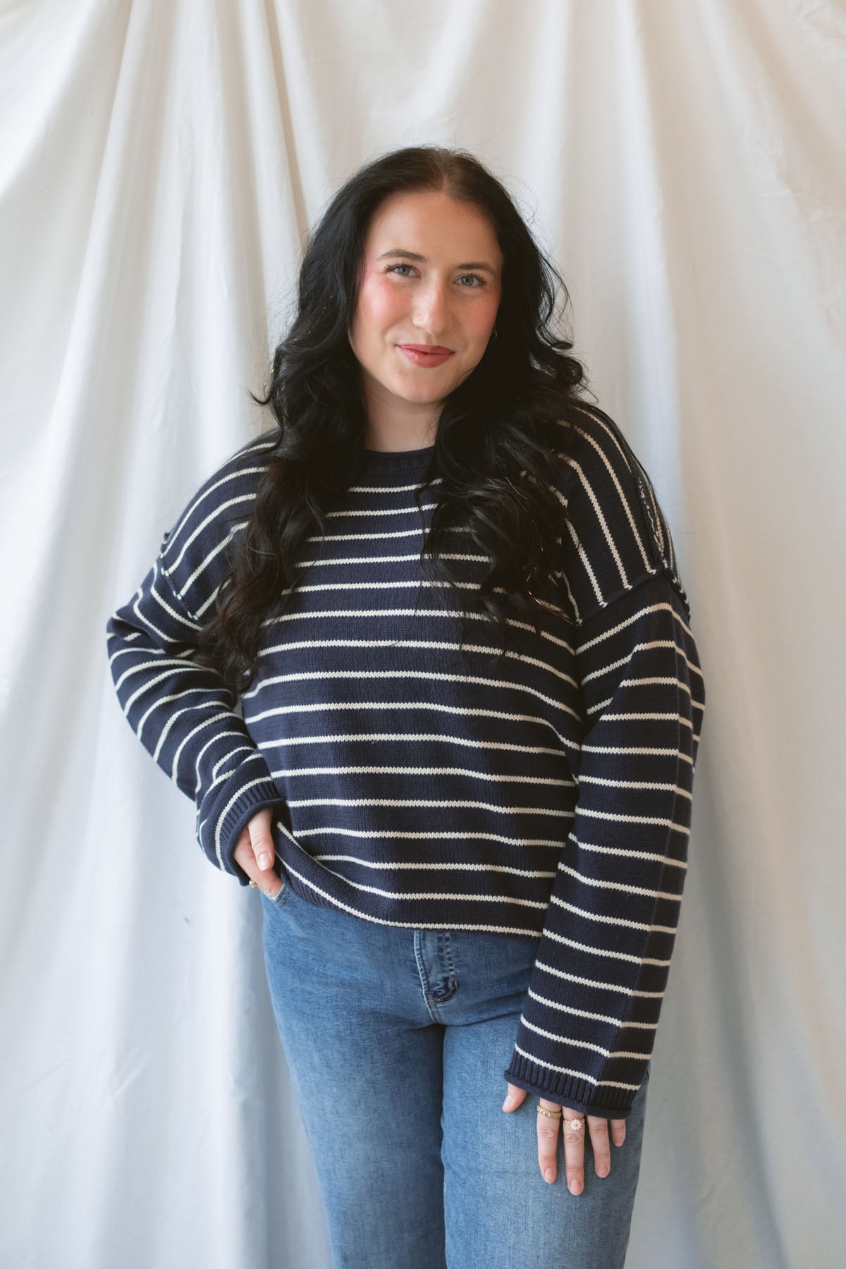 Model wearing striped crew neck sweater with raw edge detail. 