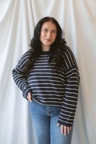 Model wearing striped crew neck sweater with raw edge detail. 