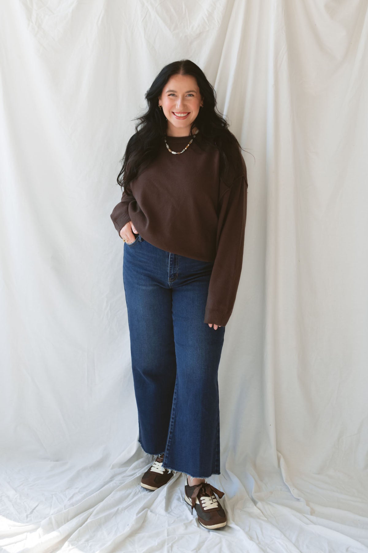 Model wearing the boat neck raw edge pullover sweater in espresso brown. Warm and cozy. Model paired the sweater with a dark denim and brown shoe for a casual and cohesive outfit. 