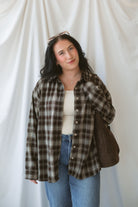 Model is wearing a long sleeve plaid button down. Styled with a square neck neutral tank and jeans.
