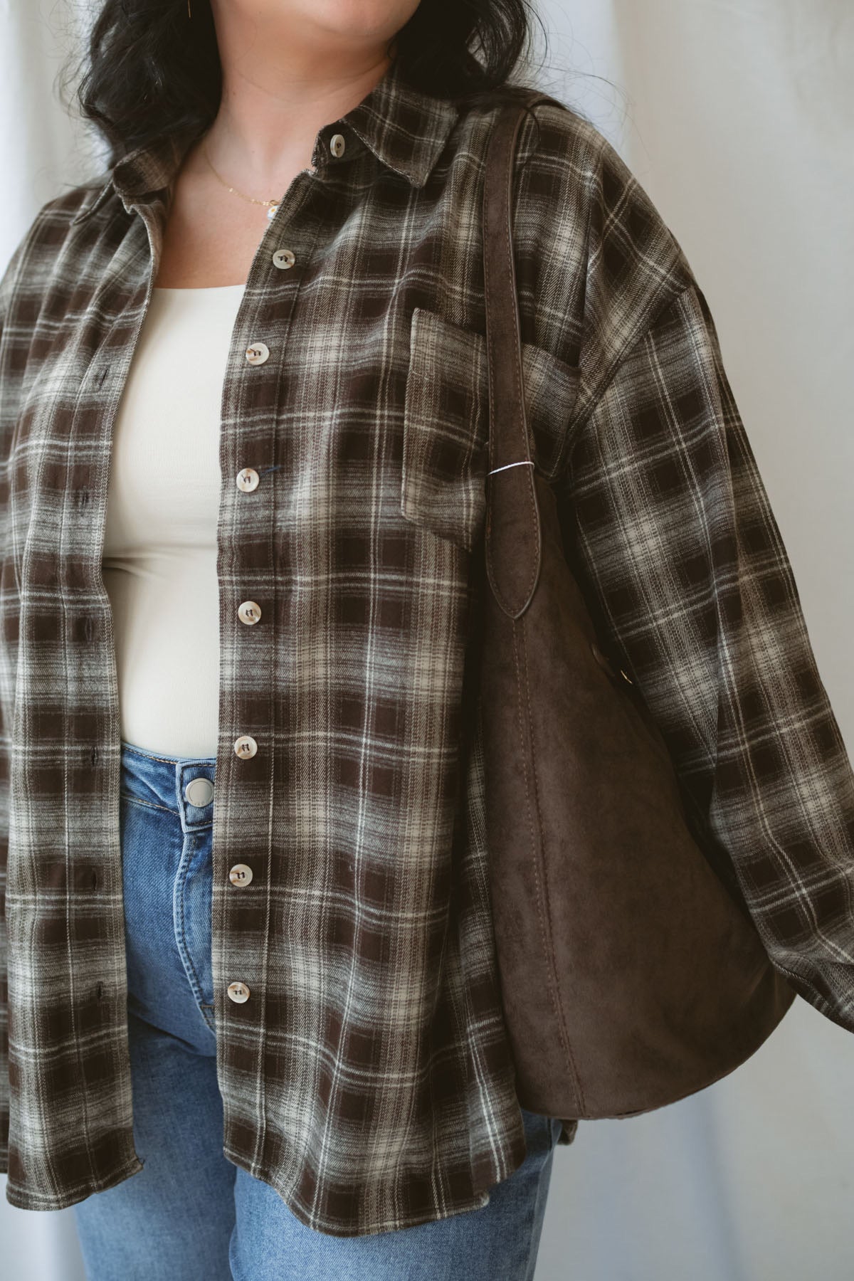 Model is wearing a long sleeve plaid button down. Styled with a square neck neutral tank and jeans.