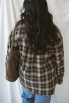 Model is wearing a long sleeve plaid button down. Styled with a square neck neutral tank and jeans.
